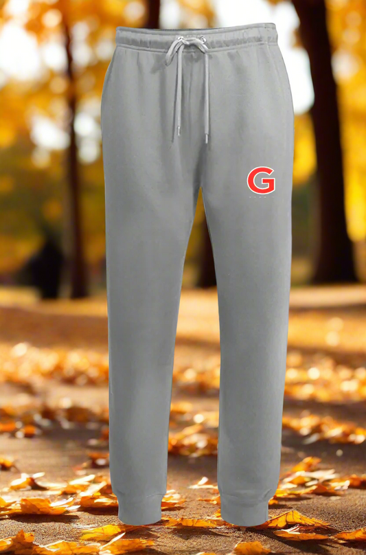 A pair of gray joggers with a drawcord waistband, featuring a small red 'G' logo on the upper left leg, presented in a Christmas-themed setting with a blurred Christmas tree and gifts in the background.